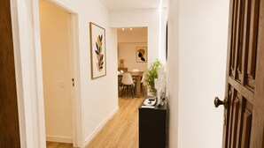 Een gang die leidt naar een eetruimte met een houten vloer, een zwarte console tafel met een vaas en een telefoon, en twee ingelijste kunstwerken aan de wanden.