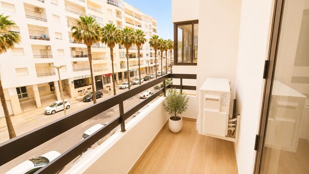 Een balkon met een bloempot, een magnetron en uitzicht op een straat met auto's en palmbomen.