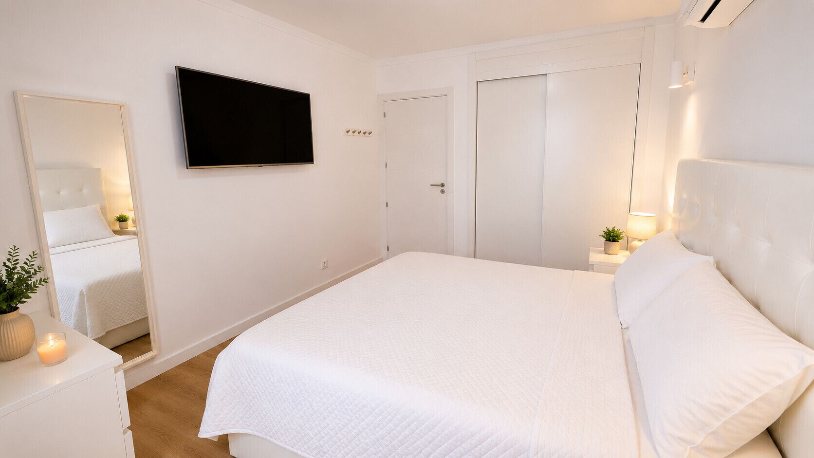 Une chambre à coucher avec un lit, un téléviseur fixé au mur, une porte et une table de chevet avec une lampe.