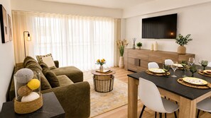 A modern living room with a sofa, coffee table, and dining area with a TV mounted on the wall. - ATLANTIC BEACH APARTMENT (Quarteira)
