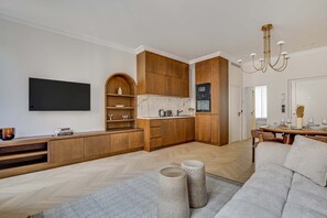 A modern living room with a flat-screen TV, a sofa, and a dining area with a table set for four. - Superbe Apartment Saint Honoré Elysée Palace (Paris)