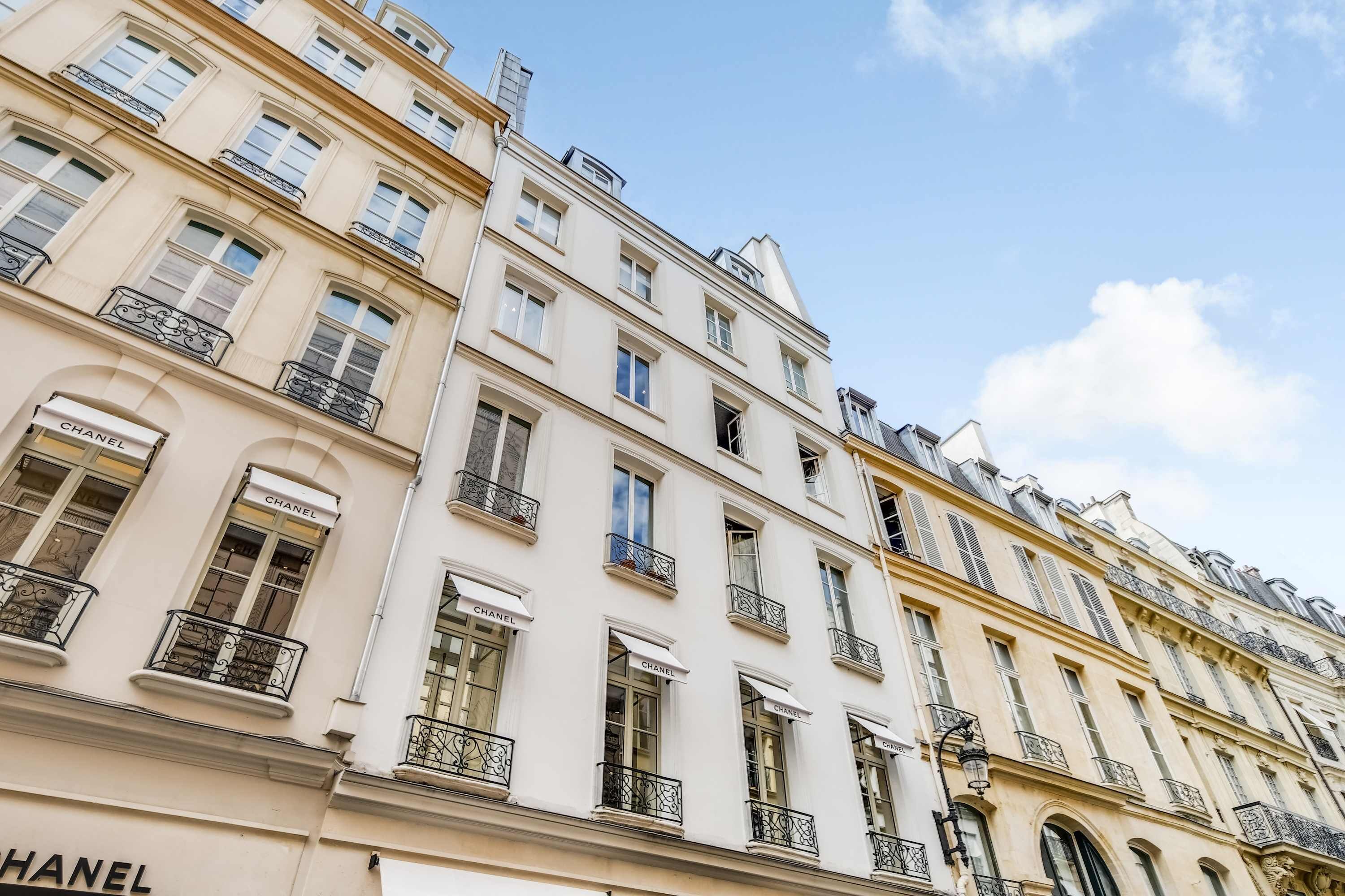 Un immeuble à plusieurs étages, doté de nombreuses fenêtres et de balcons, et abritant notamment une boutique Chanel bien en vue au rez-de-chaussée.