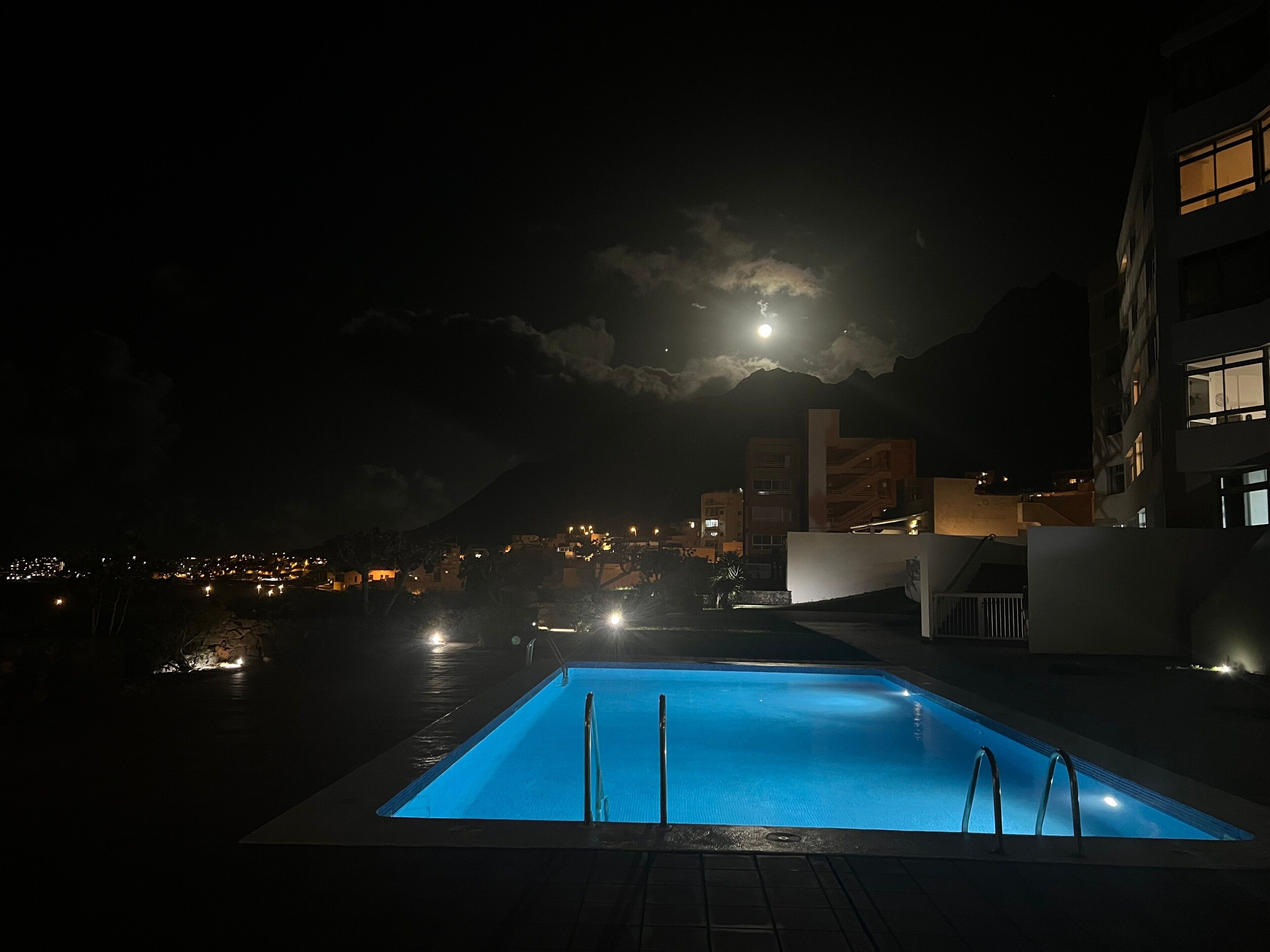 Une piscine nocturne offrant une vue sur le paysage urbain et, au loin, sur une montagne.