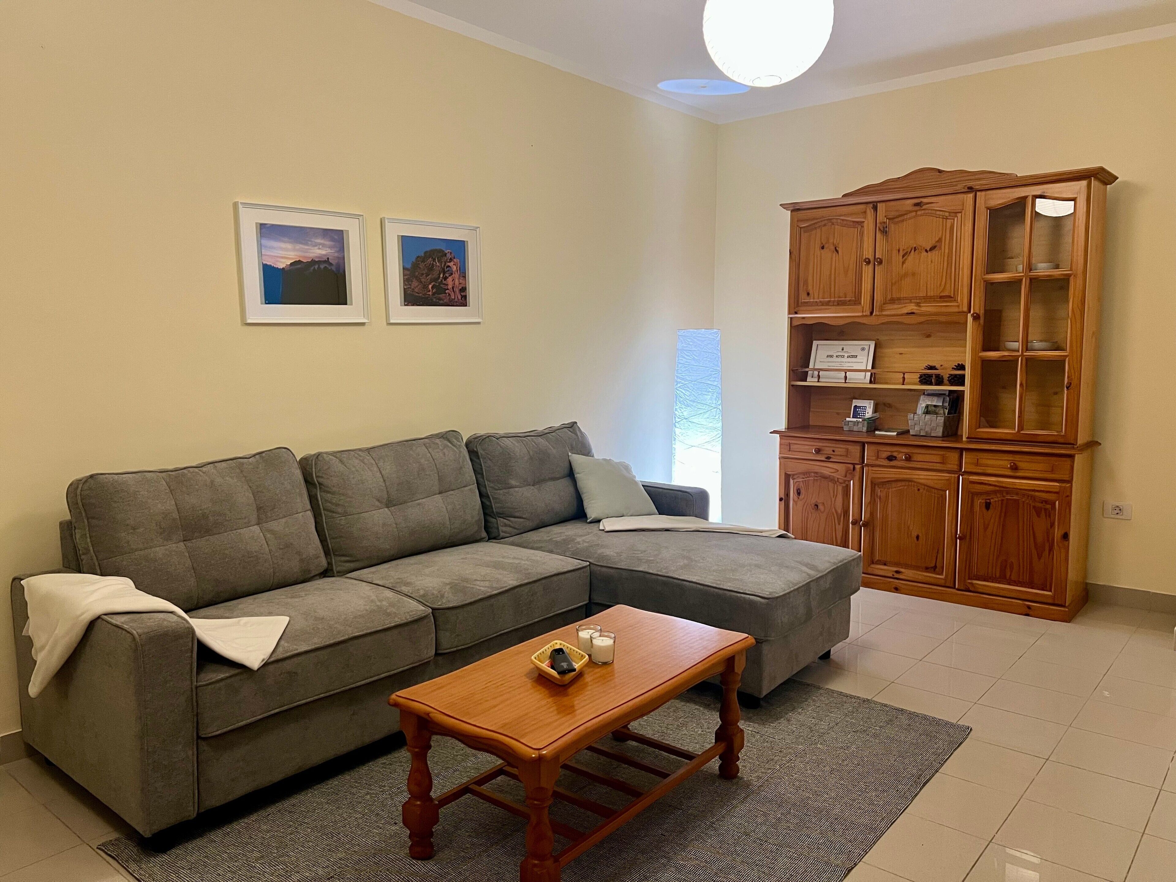 Una sala de estar con un sofá seccional gris, un mueble de madera y dos cuadros en la pared.