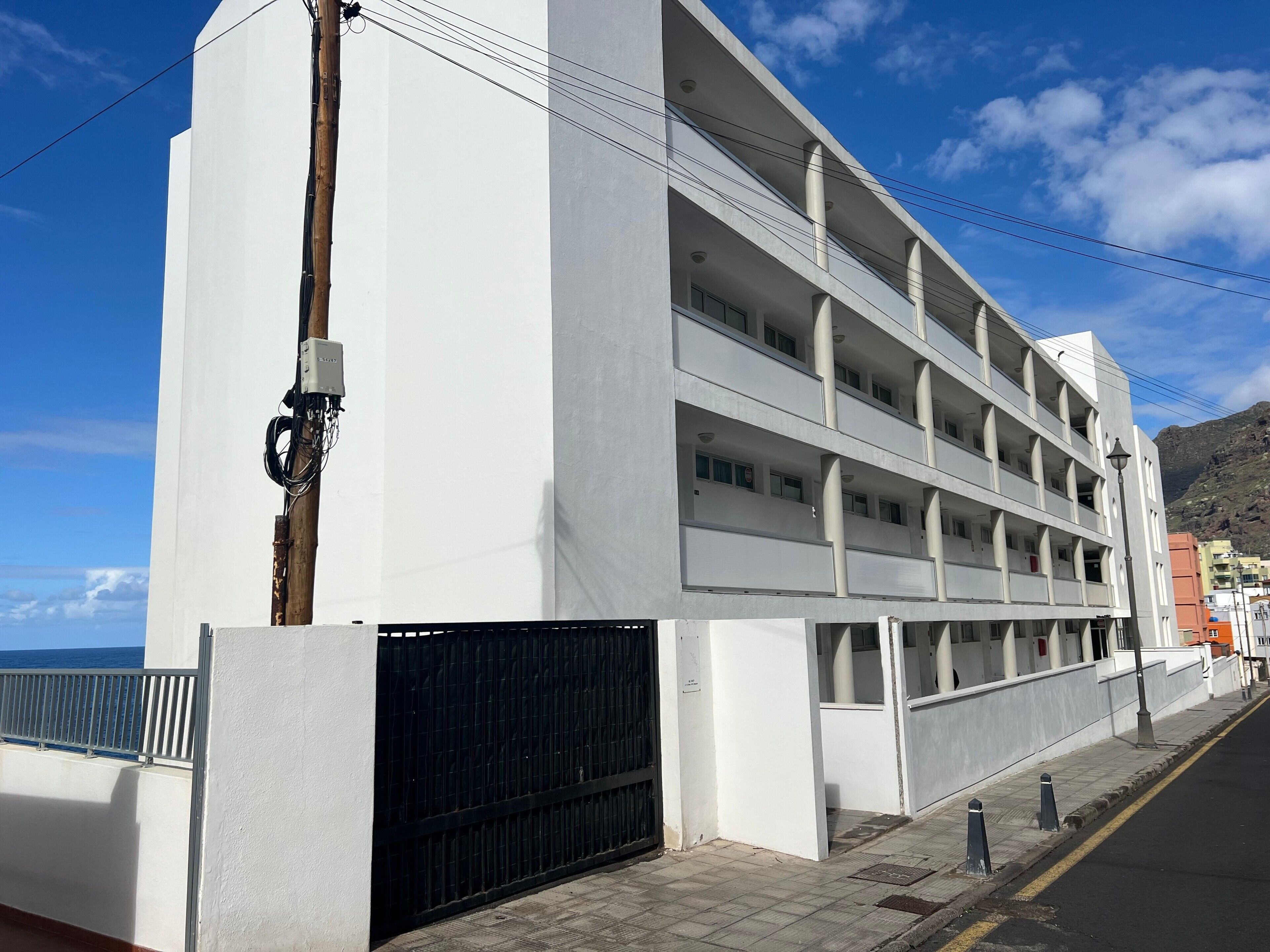 A multi-story building with balconies, a gated entrance, and a clear view of the sea.