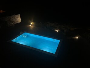 Ein rechteckiger Pool mit einer Leiter an einer Seite, umgeben von Steinmauern und kleinen Lichtern.