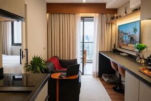 Habitación de hotel moderna con cama, escritorio con una computadora portátil, televisor y balcón con cortinas.