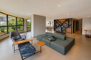 A modern living room with a grey sofa, a wooden coffee table, and a grey armchair. There is a large window providing a view of greenery outside. - Luxury apartment on the 25th floor with parking space and close to the Brooklyn Metro station. (São Paulo)