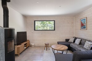 Ein modernes Wohnzimmer mit Kamin, einer Couch, einem Fernseher und einem Fenster mit Blick auf Bäume.