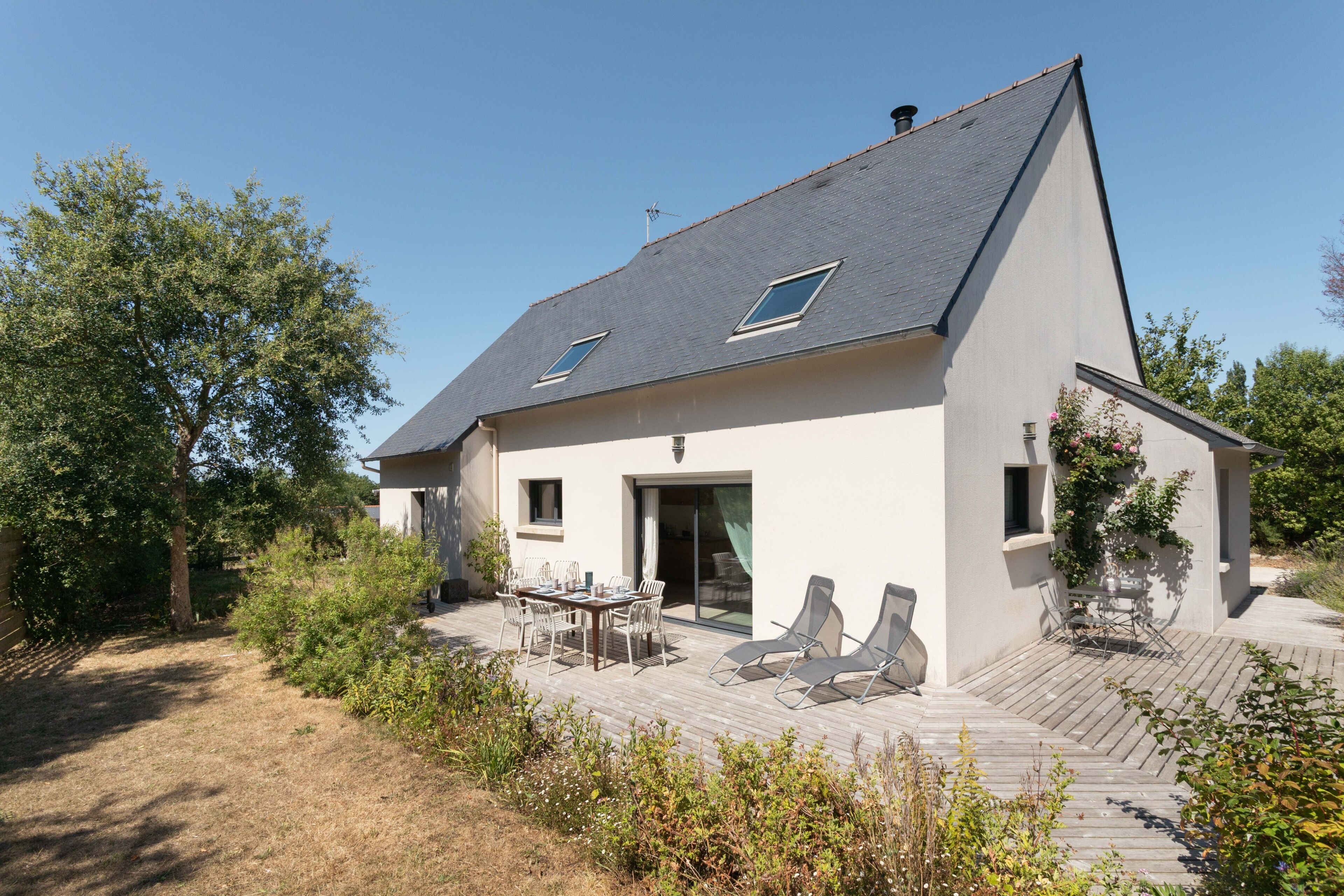 A modern house with a sloped roof, a covered patio with outdoor furniture, and a garden area.