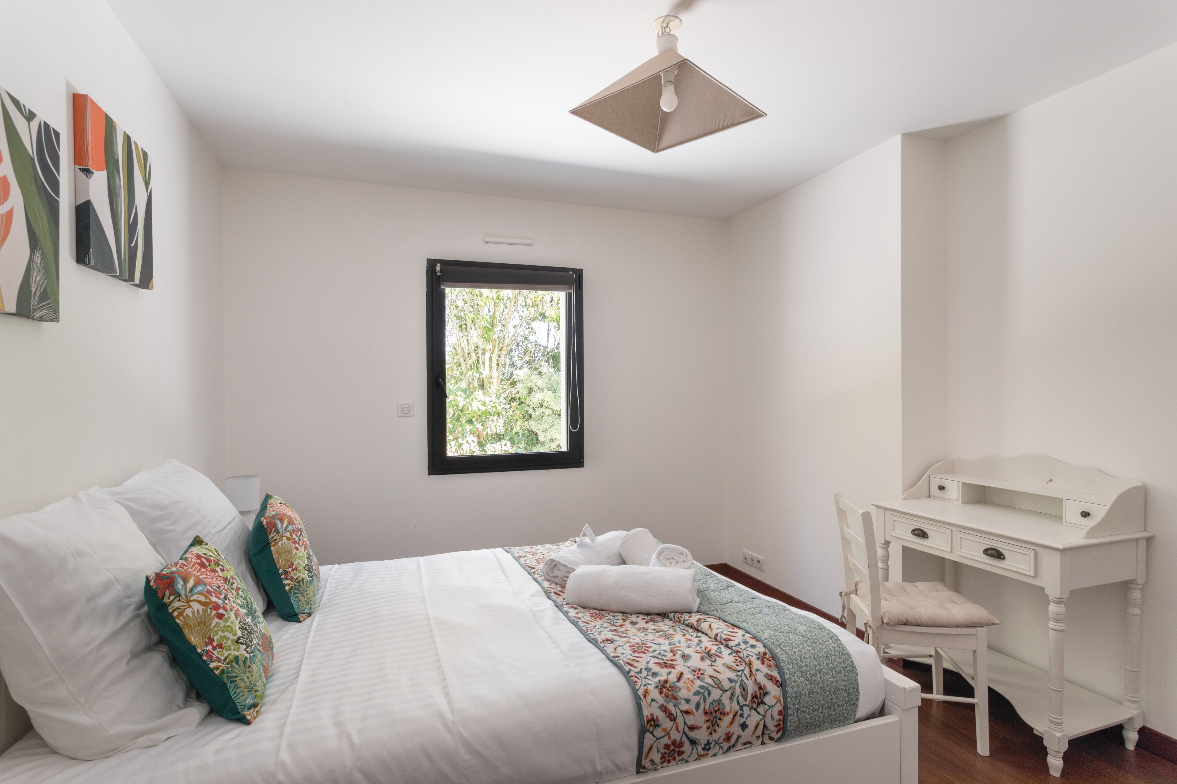A bedroom with a bed, a desk, and a window.