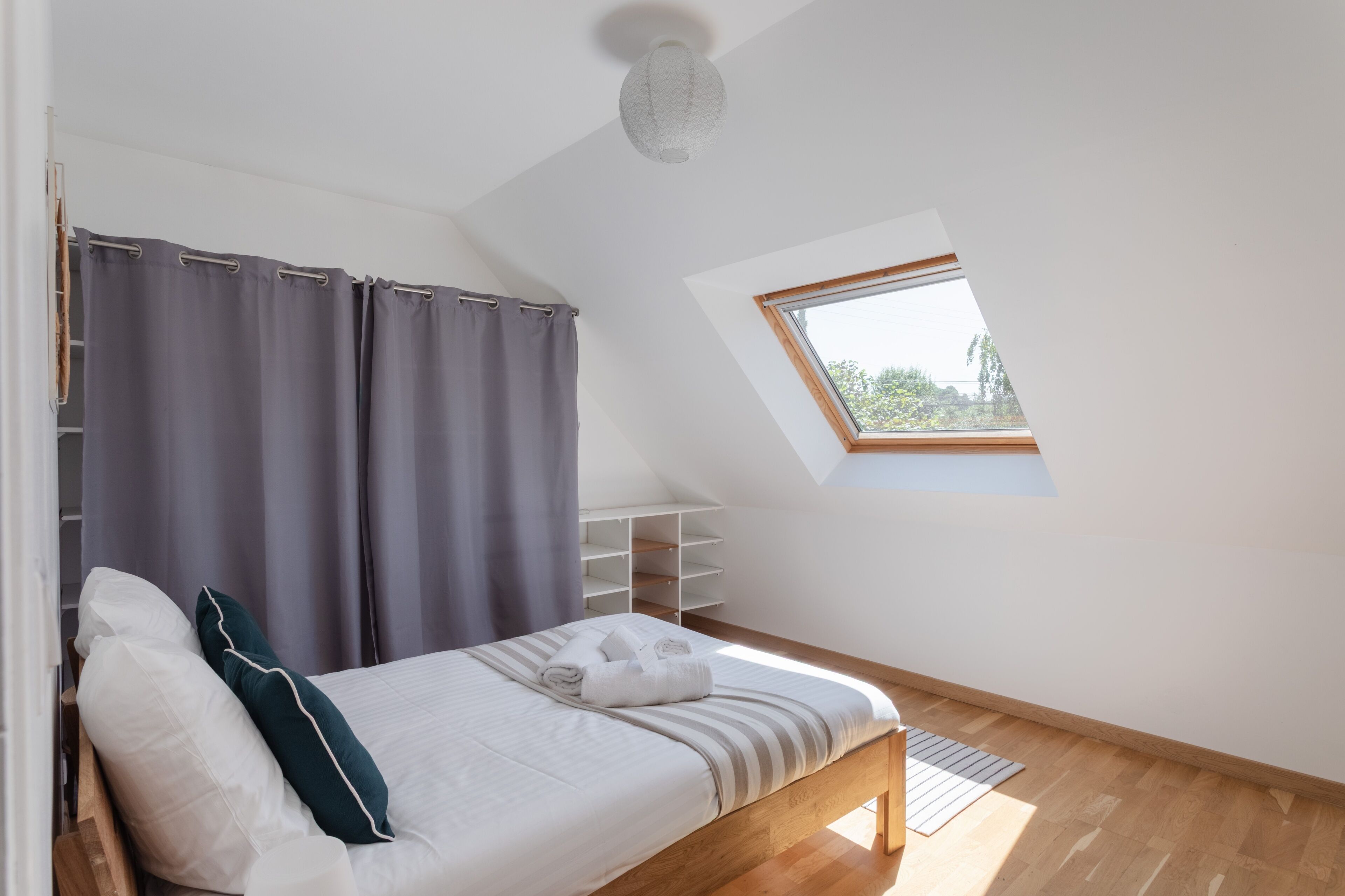 Une chambre avec un plafond en pente, un puits de lumière, un lit avec une literie blanche et un plancher en bois.