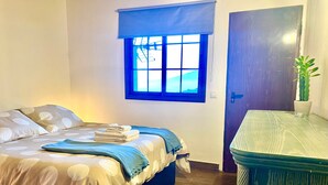 Ein Schlafzimmer mit einem Bett, einem Fenster, einer Tür und einem kleinen Tisch mit einer Pflanze.