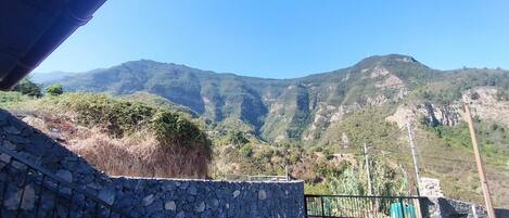 Un muro de piedra con barandilla metálica, vista de un paisaje montañoso y cielo despejado.