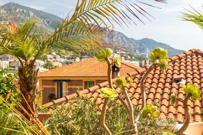 A building with a tiled roof, surrounded by greenery and mountains in the background. - Le Lemon Tree - Terrasse avec vue sur Monaco (Beausoleil)