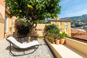 A balcony with a lounge chair, potted plants, and a view of a cityscape. - Le Lemon Tree - Terrasse avec vue sur Monaco (Beausoleil)