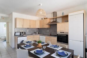 A modern kitchen with wooden cabinets, a built-in oven, and a dining area set for a meal. - Pieta - À moins de 100 m du port (Cancale)