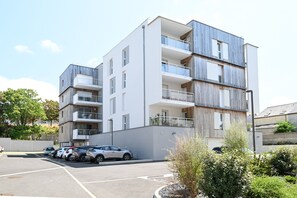 A multi-story residential building with balconies, a parking lot, and surrounding greenery. - Chez Nathalie - Appt avec terrasses proche plage (Donville-les-Bains)