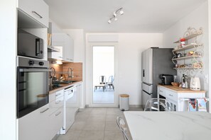 A modern kitchen with stainless steel appliances, a wooden countertop, and a view into the dining area. - Chez Nathalie - Appt avec terrasses proche plage (Donville-les-Bains)
