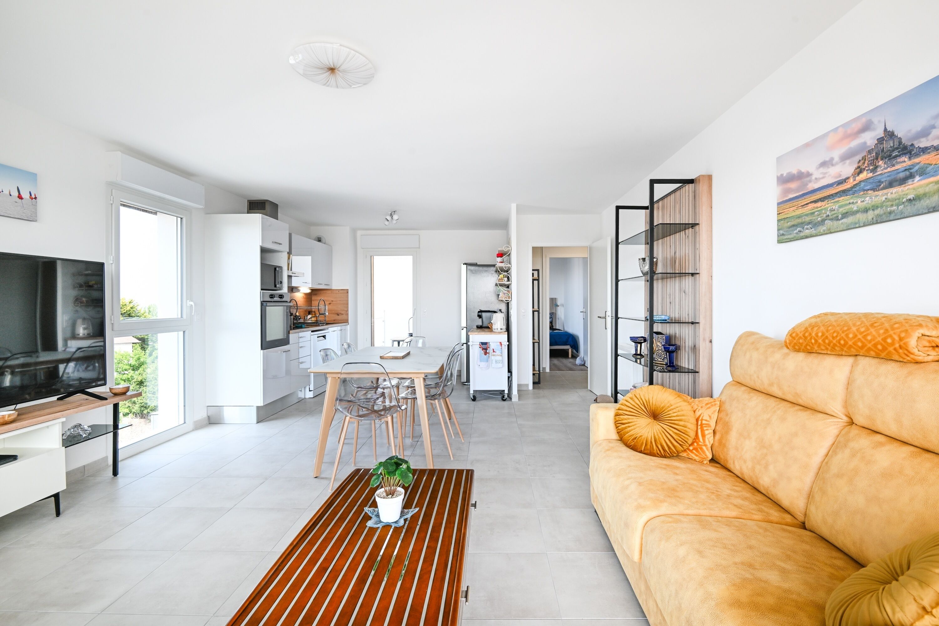A modern living room with a sofa, a television, and a dining area with chairs and a table.