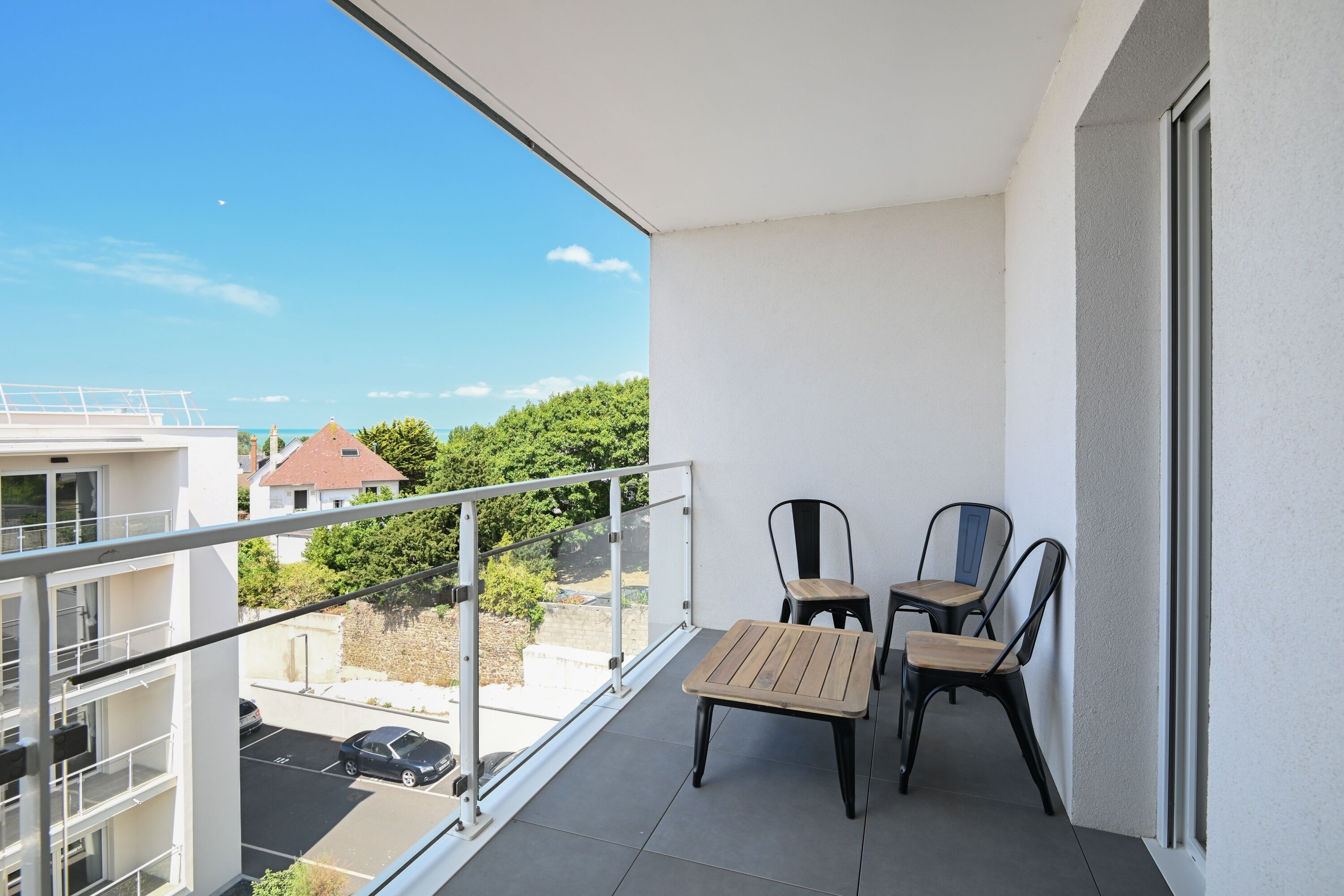 A balcony with a table and chairs, a view of the street, and a building in the background.