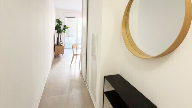 Een hal met een ronde spiegel aan de muur, een zwarte console tafel en een plant in de verte.