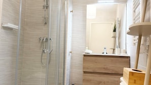 Een moderne badkamer met een glazen douchecabine, een toilet, een wastafel met spiegel en een kleine plant op een plank.