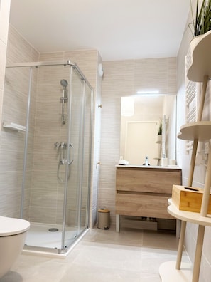 A modern bathroom with a glass-enclosed shower, a toilet, a vanity with a mirror, and a small plant on a shelf. - INFINICE AP4514 by Riviera Holiday Homes (Nice)