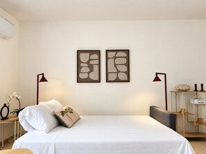 Ein Schlafzimmer mit einem Bett, zwei Wandlampen, einem kleinen Tisch mit einer Vase und einem Regal mit Dekorationen.