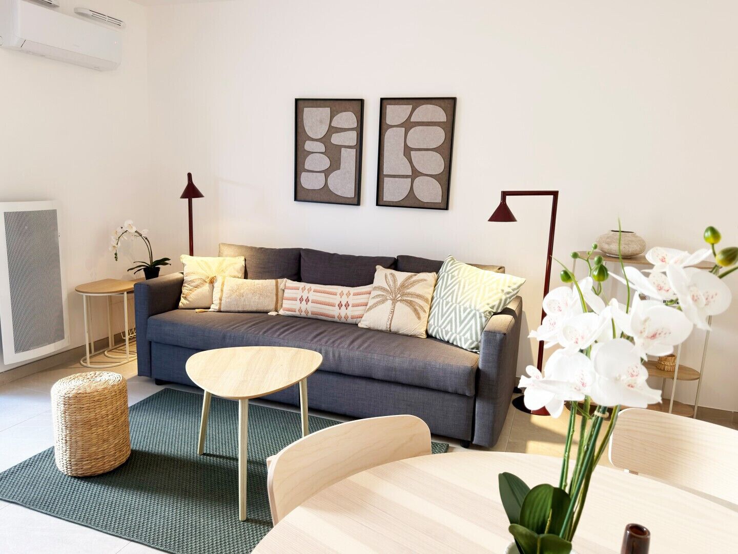 Un salon moderne avec un canapé gris, une table basse ronde en bois et une petite table d’appoint avec une lampe.