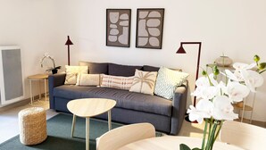 Een moderne woonkamer met een grijze bank, een ronde houten salontafel en een bijzettafeltje met een lamp.