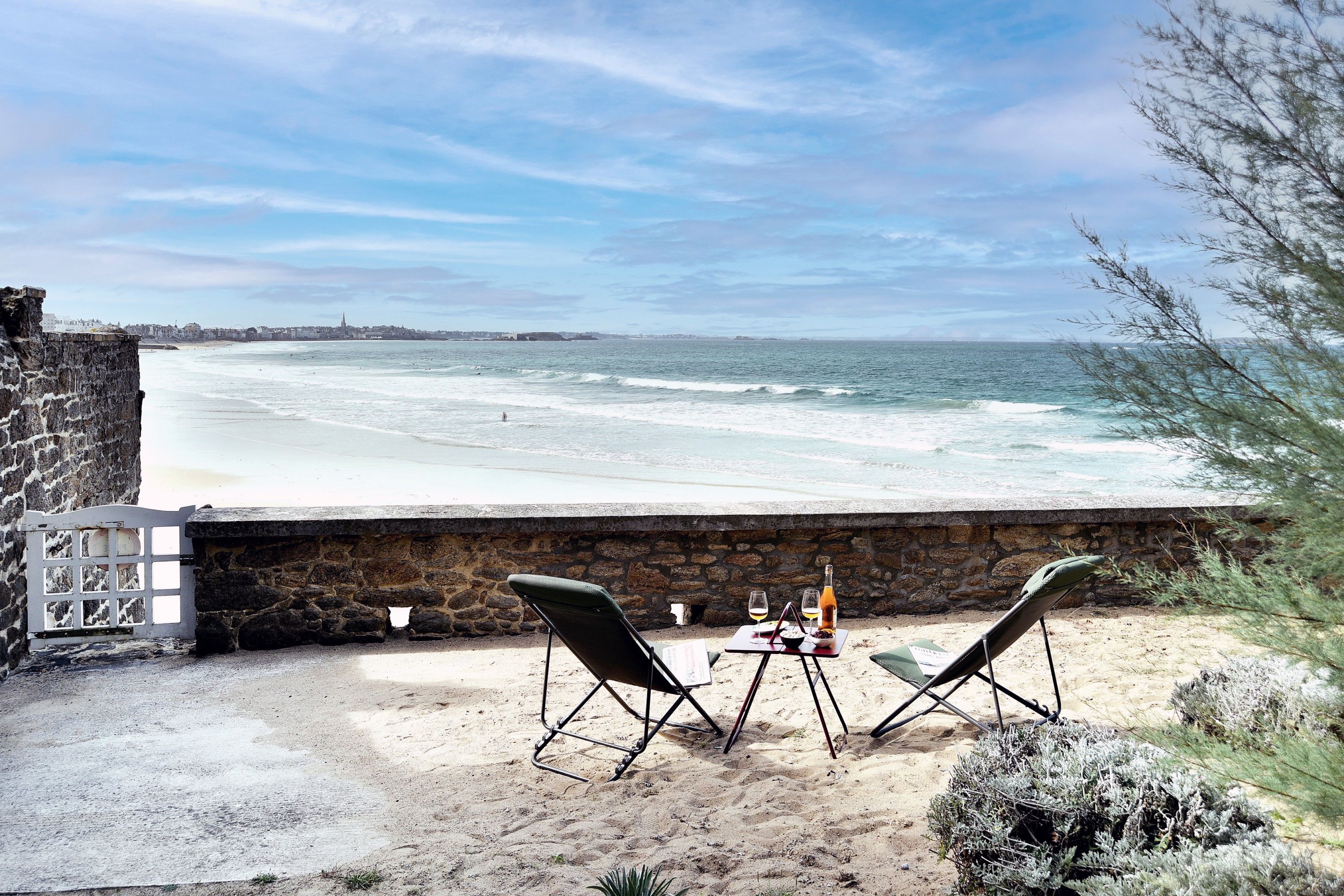 Une terrasse au bord de la plage, avec deux chaises et une table, d’où l’on peut admirer une plage de sable et la mer.