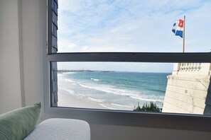 Blick aus dem Fenster auf einen Strand mit Wellen, einer Flagge und einem Gebäude.