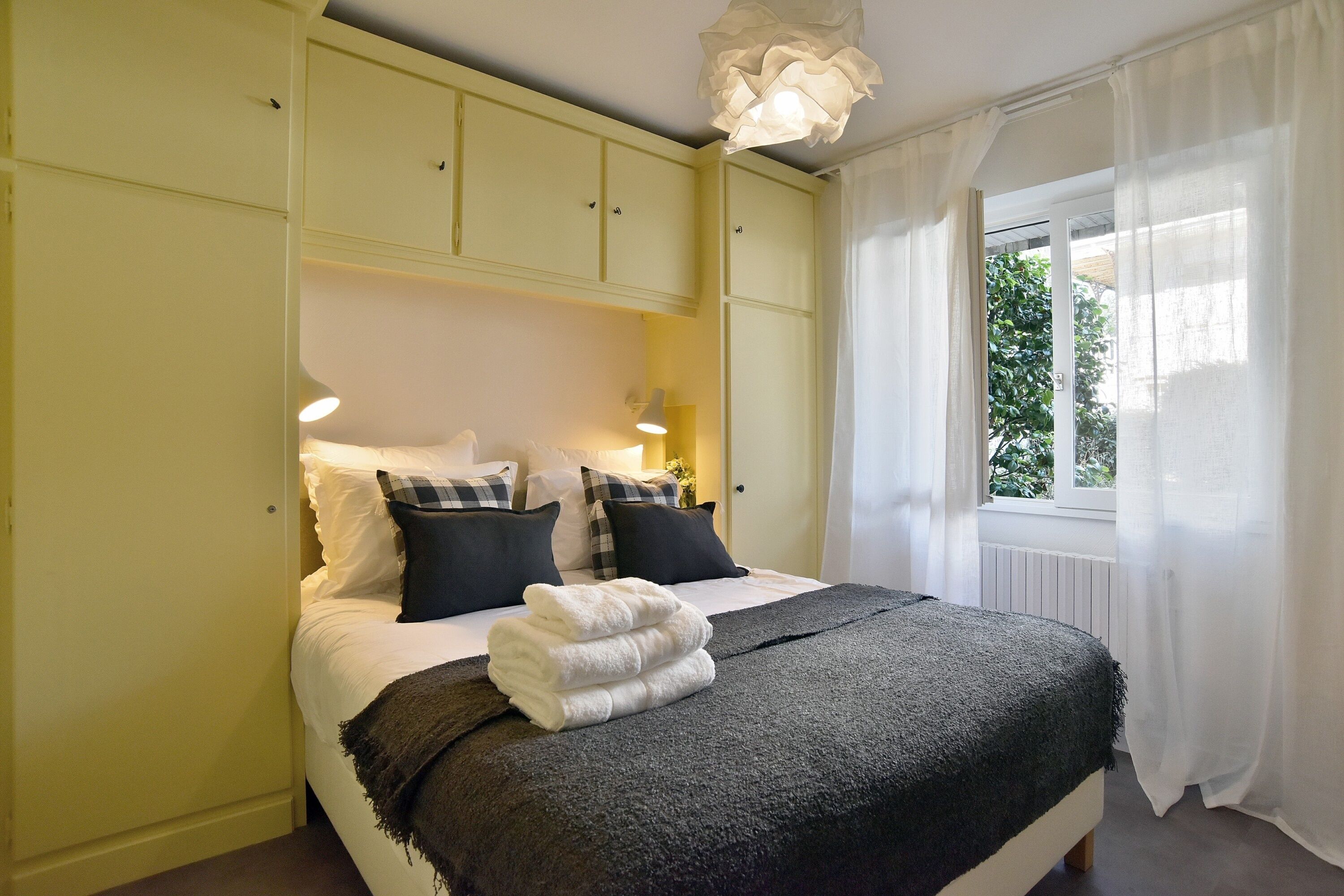 Un dormitorio con cama, almohadas, una colcha y una ventana con cortinas.