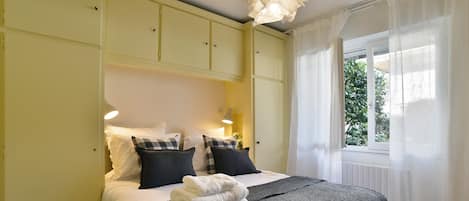 Un dormitorio con cama, almohadas, una colcha y una ventana con cortinas.