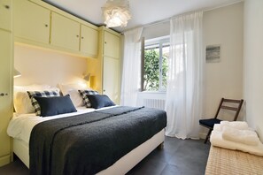 A bedroom with a bed, pillows, a window with curtains, a chair, and a wall-mounted light fixture. - Ciel & Mer - Avec vue imprenable sur la mer (Saint-Malo)