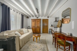 A living room with a sofa, a coffee table, a dining table with chairs, a wooden wardrobe, and a mirror on the wall. - Le Charme - Studio avec Parking (Janvry)