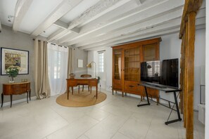 A room with a wooden ceiling, a television on a stand, a wooden cabinet, and a desk with a chair. - Le Charme - Studio avec Parking (Janvry)