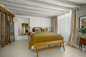 Un dormitorio con cama, un banco, un espejo, una cómoda y un cuadro.