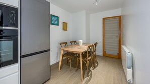 A compact kitchen with a built-in refrigerator, a dining table with chairs, and a door with a roller shutter. - Le Cèdre - Studio avec Parking (Janvry)