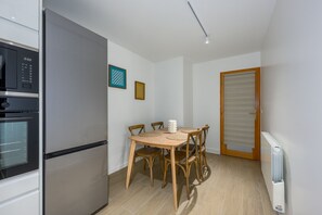 Cuina compacta amb nevera integrada, taula de dinar amb cadires i una porta amb persianes.