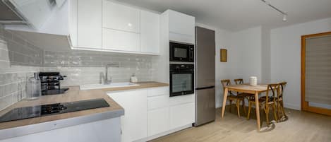 A modern kitchen with white cabinetry, a built-in oven, and a dining area with wooden chairs and a table.
