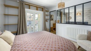 A bedroom with a bed, a window with curtains, a radiator, and a hanging light fixture. - Le Cèdre - Studio avec Parking (Janvry)
