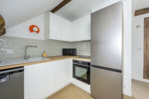 A modern kitchen with white cabinets, a stainless steel refrigerator, a microwave, and a dishwasher. - Le Chêne - Studio avec Parking (Janvry)