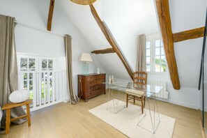 A room with a sloped ceiling, wooden beams, a glass table, a wooden chair, a dresser, and a window with curtains. - Le Chêne - Studio avec Parking (Janvry)