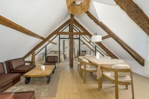 A loft bedroom with a sloped ceiling, wooden beams, a sofa, a table, and a bed. - Le Chêne - Studio avec Parking (Janvry)