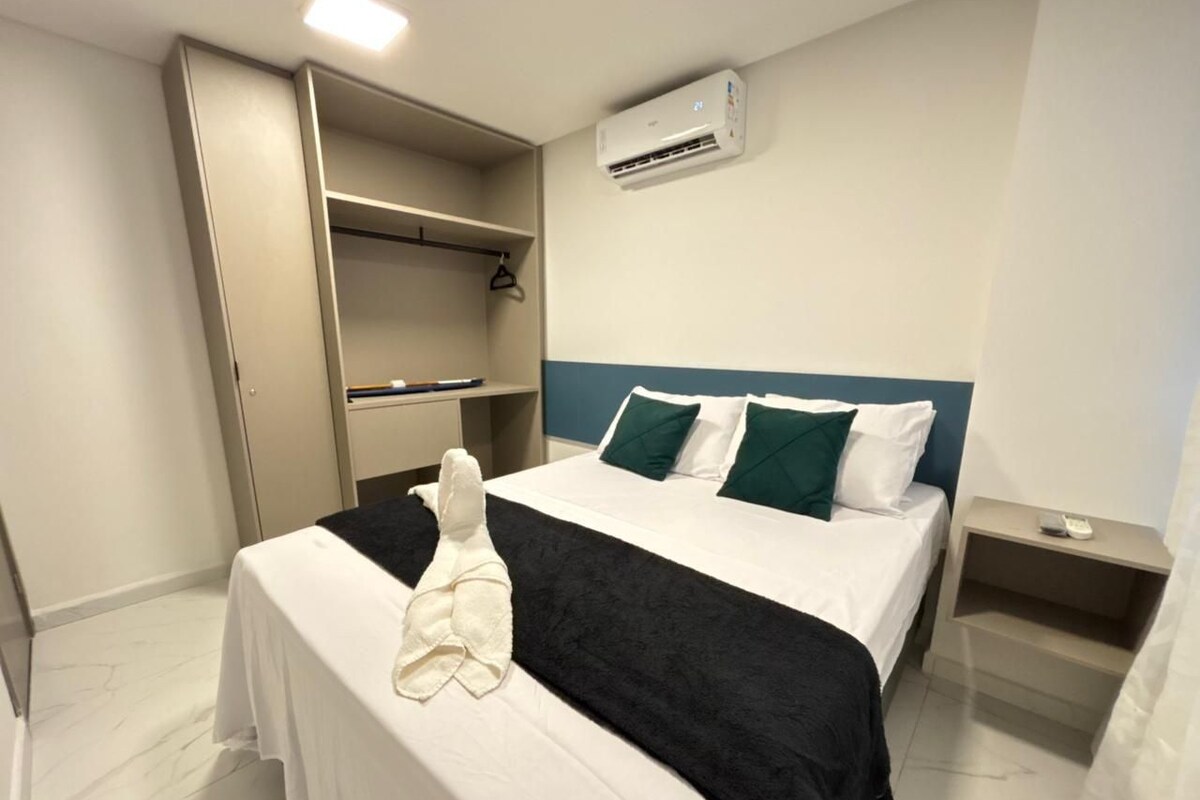 A hotel room with a bed, a wardrobe, a nightstand, and an air conditioning unit.