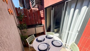A small outdoor dining area with a round table set for four, surrounded by chairs, a wooden fence, and a sliding glass door leading to an indoor space. - Smeralda del Mare Residence - Porto de Galinhas (Ipojuca)