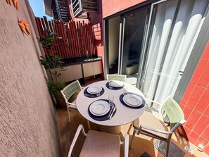 A small outdoor dining area with a round table set for four, surrounded by chairs, a wooden fence, and a sliding glass door leading to an indoor space. - Smeralda del Mare Residence - Porto de Galinhas (Ipojuca)