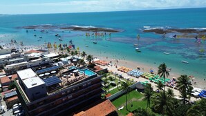 A coastal hotel with a rooftop pool, beachside umbrellas, and a view of the sea. - Smeralda del Mare Residence - Porto de Galinhas (Ipojuca)